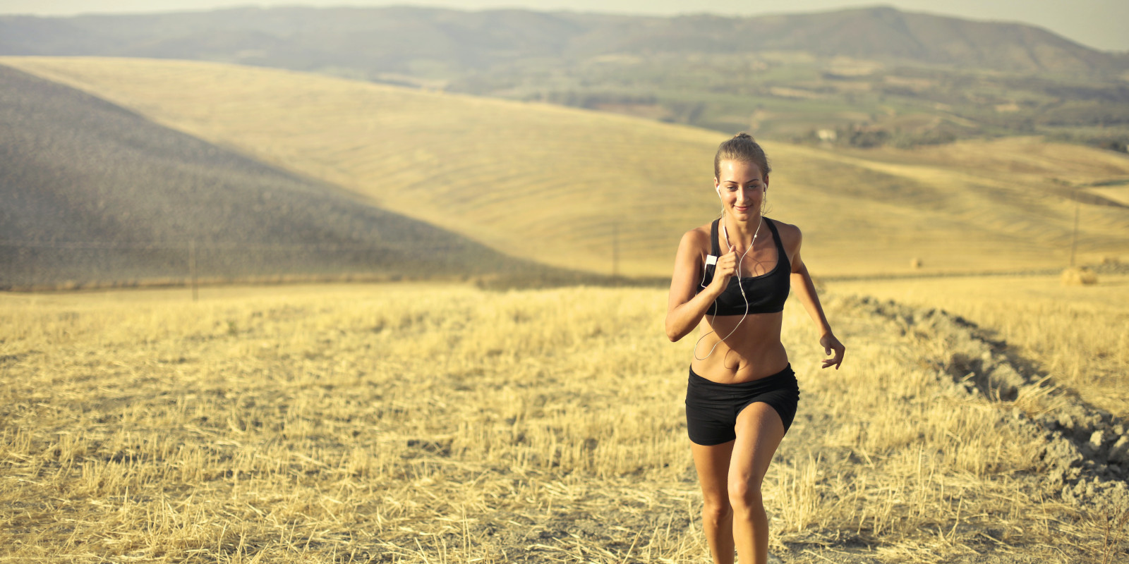 Photo by Andrea Piacquadio via Pexels, showing a cheerful sportswoman running along hill in summer